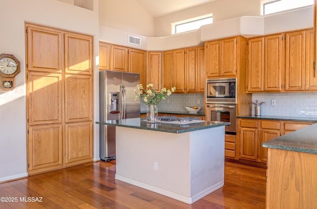 kitchen with decorative backsplash, a center island, stainless steel appliances, and a high ceiling