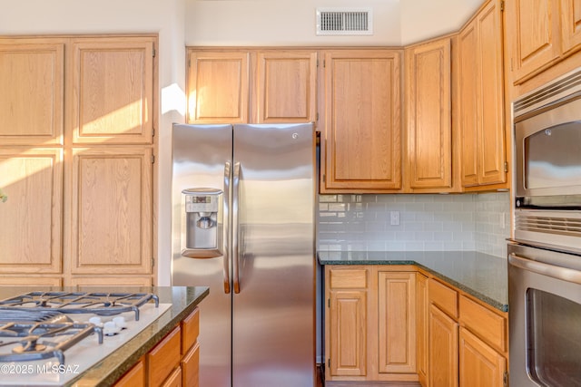 kitchen featuring decorative backsplash, light brown cabinetry, stainless steel appliances, and dark stone counters