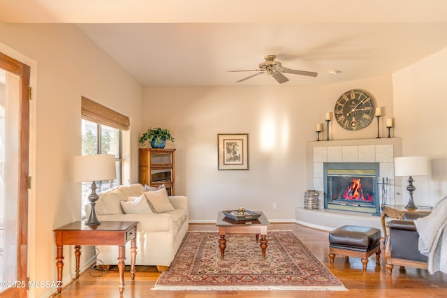 living room with a tiled fireplace, ceiling fan, and wood-type flooring