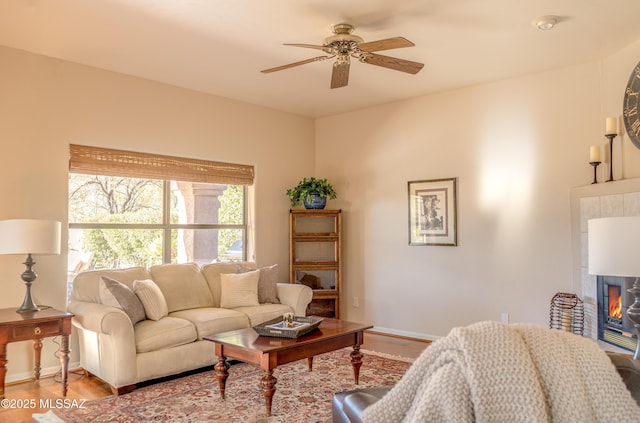 living room featuring a tile fireplace, light hardwood / wood-style floors, and ceiling fan