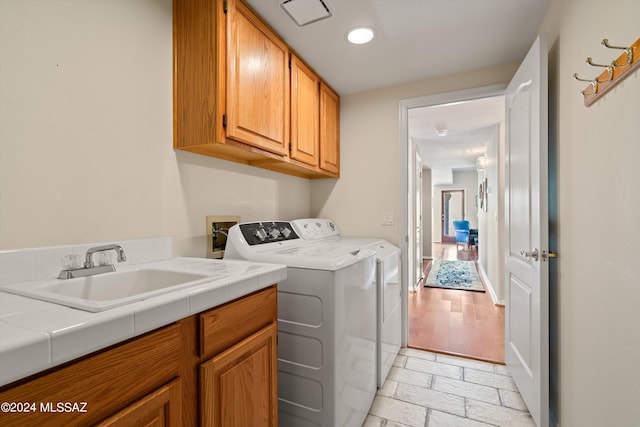 clothes washing area featuring light hardwood / wood-style flooring, cabinets, sink, and washing machine and clothes dryer