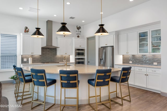 kitchen with stainless steel appliances, sink, wall chimney range hood, and white cabinets