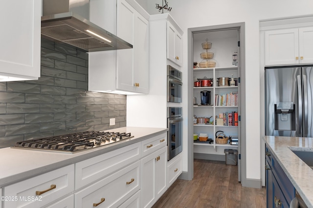 kitchen featuring white cabinetry, appliances with stainless steel finishes, wall chimney exhaust hood, and dark wood-type flooring