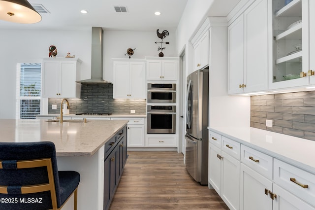 kitchen with dark hardwood / wood-style floors, white cabinets, a kitchen bar, stainless steel appliances, and wall chimney exhaust hood