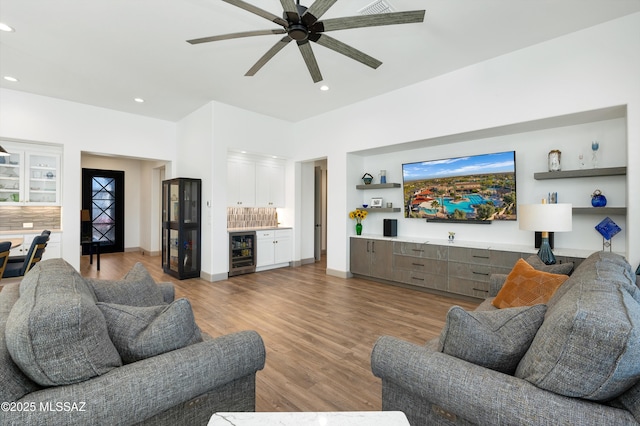 living room featuring ceiling fan, bar, beverage cooler, and light wood-type flooring