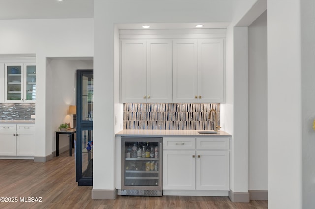 bar with sink, white cabinetry, wood-type flooring, beverage cooler, and decorative backsplash