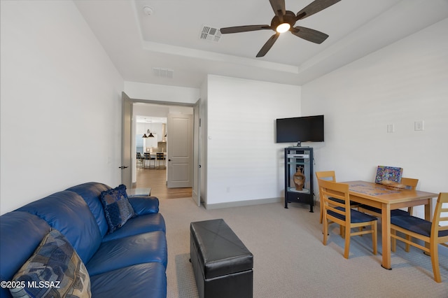 carpeted living room featuring a raised ceiling and ceiling fan