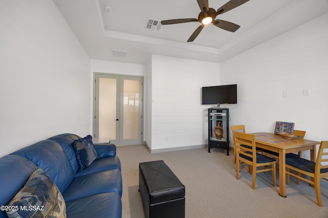 living room with a raised ceiling, light carpet, ceiling fan, and french doors