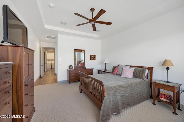 bedroom featuring light carpet, a tray ceiling, independent washer and dryer, and ceiling fan