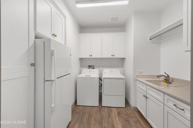 clothes washing area featuring cabinets, sink, hardwood / wood-style floors, and independent washer and dryer