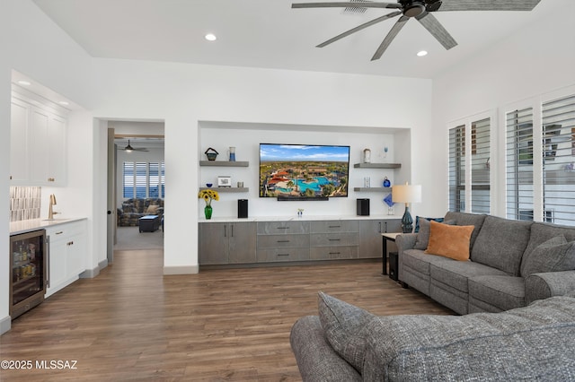 living room featuring dark wood-type flooring, indoor wet bar, beverage cooler, and ceiling fan