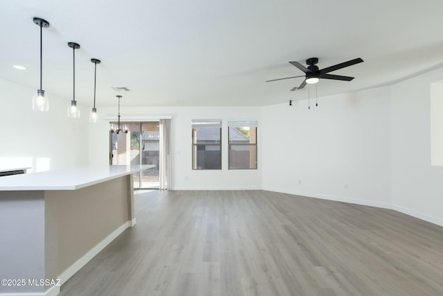 unfurnished living room featuring ceiling fan with notable chandelier, visible vents, wood finished floors, and baseboards