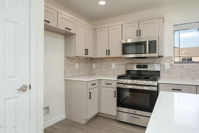 kitchen with backsplash, light stone countertops, light wood-type flooring, recessed lighting, and appliances with stainless steel finishes