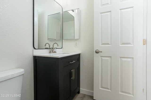 bathroom featuring baseboards, toilet, wood finished floors, and vanity