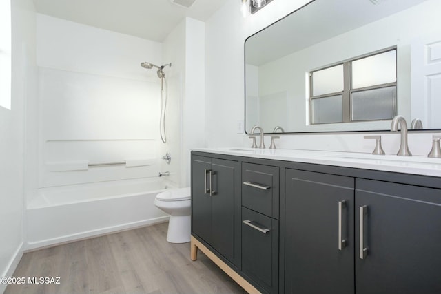 bathroom featuring washtub / shower combination, wood finished floors, double vanity, a sink, and toilet