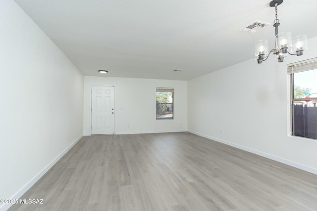 unfurnished room featuring light wood-type flooring, visible vents, a healthy amount of sunlight, and a chandelier