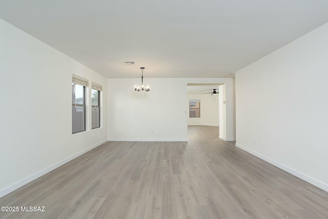 empty room featuring light wood finished floors, a notable chandelier, visible vents, and baseboards