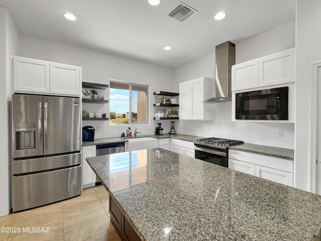 kitchen with appliances with stainless steel finishes, white cabinetry, a center island, light stone countertops, and wall chimney exhaust hood