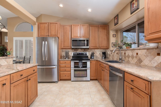 kitchen with backsplash, sink, vaulted ceiling, light stone counters, and stainless steel appliances