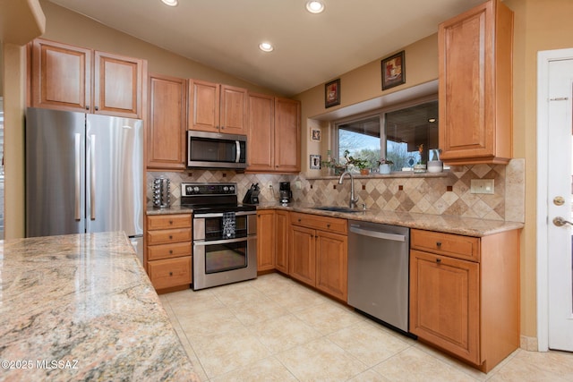 kitchen with lofted ceiling, backsplash, sink, light stone counters, and stainless steel appliances