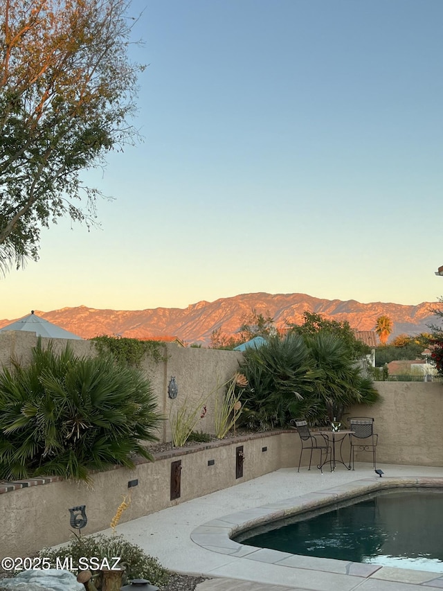 pool at dusk featuring a patio area and a mountain view