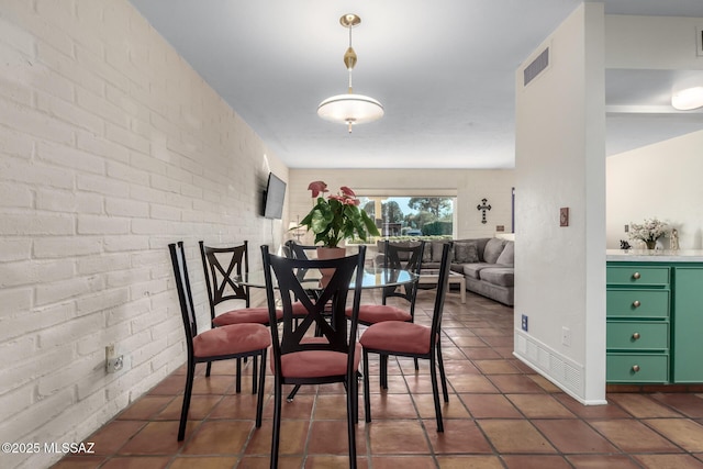 dining room featuring dark tile patterned flooring and brick wall