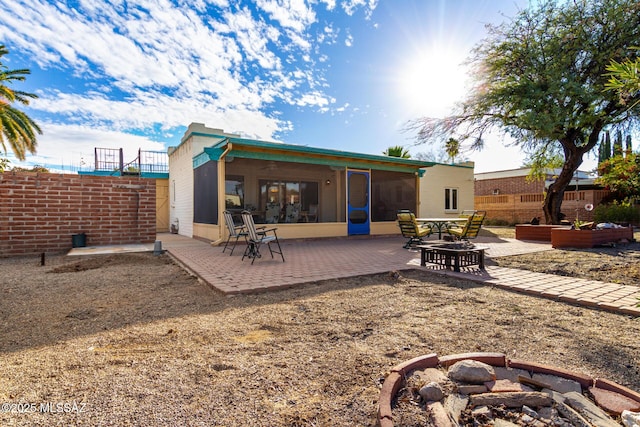 back of house with a sunroom, a patio area, and an outdoor fire pit