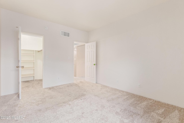 unfurnished bedroom with light carpet, a spacious closet, and a closet