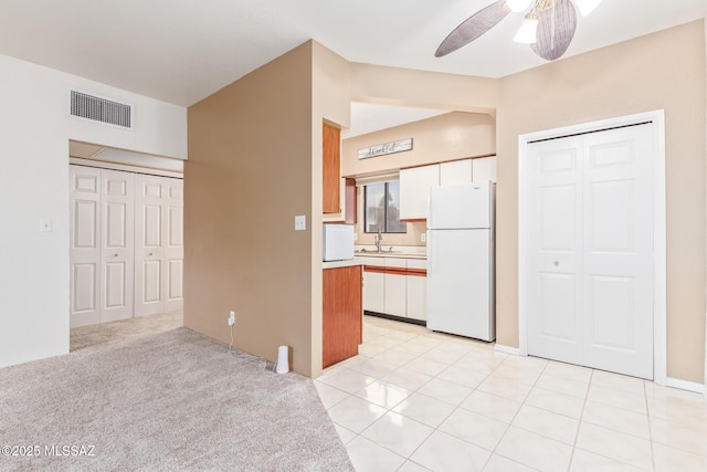 kitchen featuring ceiling fan, sink, white refrigerator, light carpet, and white cabinets