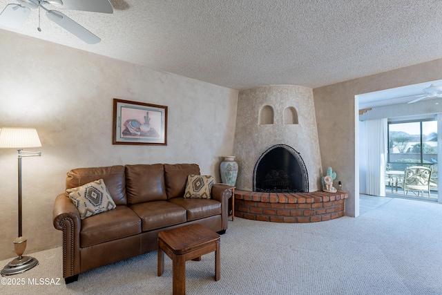 carpeted living room with a textured ceiling, ceiling fan, and a large fireplace