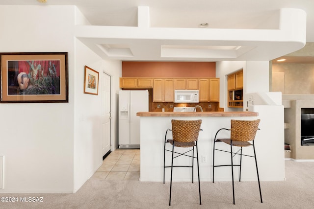 kitchen featuring tasteful backsplash, white appliances, a breakfast bar area, light carpet, and light brown cabinetry