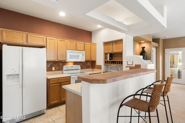 kitchen with a kitchen breakfast bar, tasteful backsplash, white appliances, a center island with sink, and light tile patterned flooring