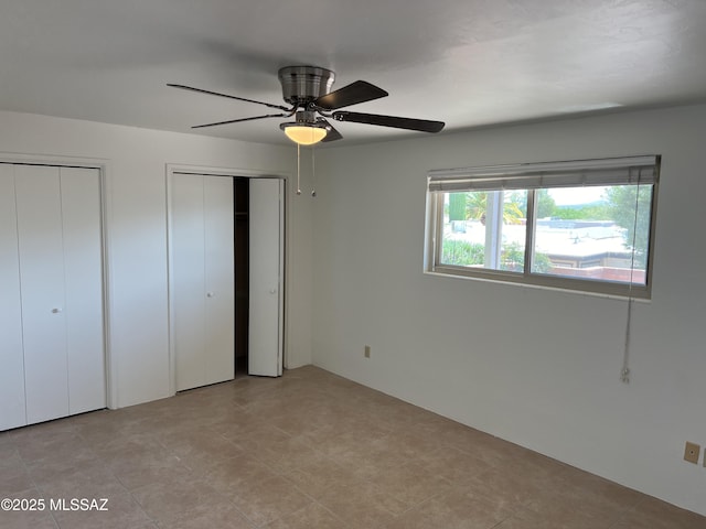 unfurnished bedroom featuring ceiling fan and multiple closets