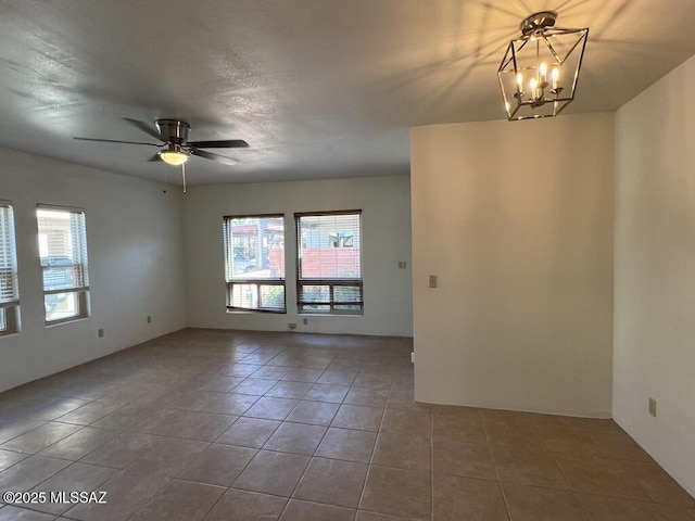 tiled empty room featuring ceiling fan with notable chandelier and a healthy amount of sunlight