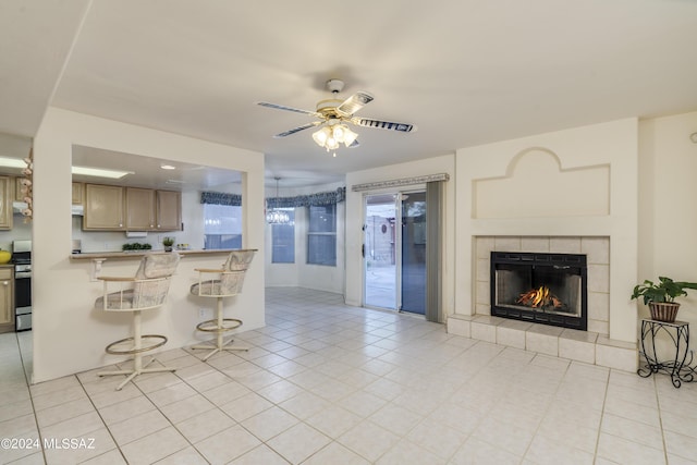 kitchen featuring ceiling fan, stainless steel range, a breakfast bar area, a fireplace, and light tile patterned flooring