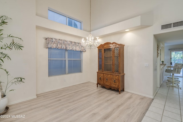 spare room featuring a chandelier, a high ceiling, and light hardwood / wood-style flooring