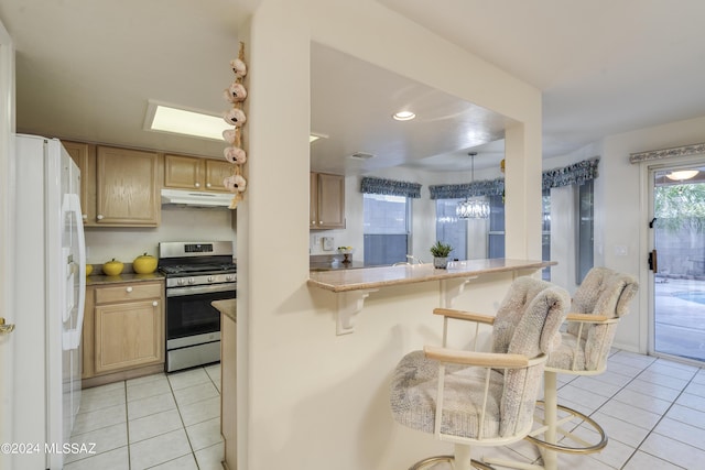 kitchen featuring a kitchen bar, kitchen peninsula, white fridge, stainless steel range with gas cooktop, and light tile patterned flooring