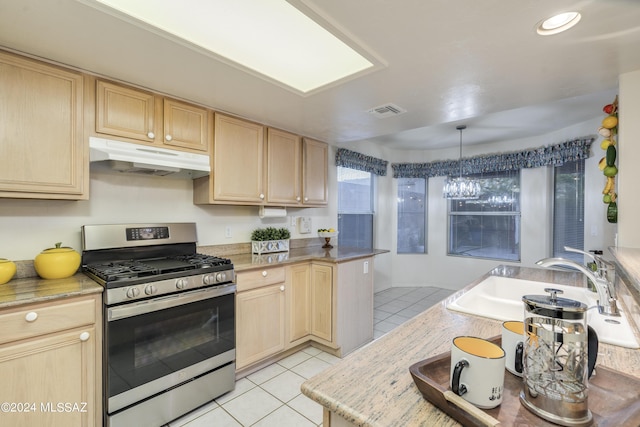 kitchen with hanging light fixtures, sink, stainless steel gas range, light tile patterned floors, and light brown cabinetry