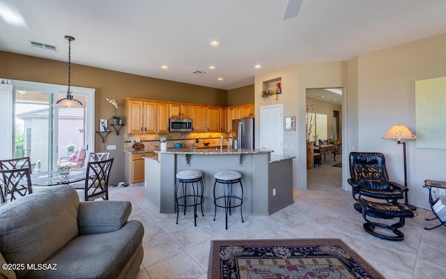 kitchen with light stone counters, an island with sink, a breakfast bar area, decorative backsplash, and appliances with stainless steel finishes