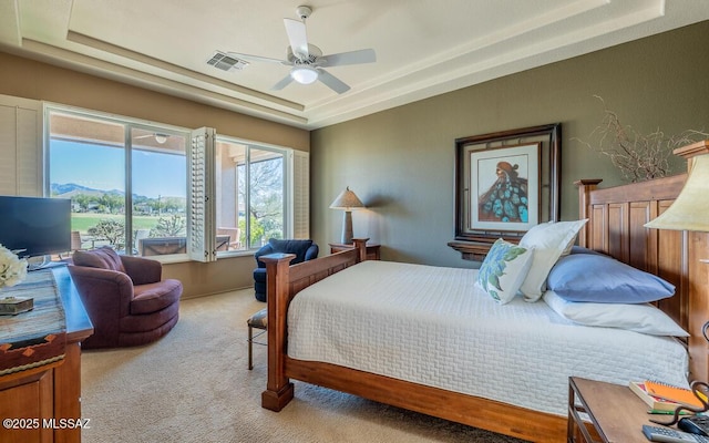 bedroom featuring light carpet, a tray ceiling, and ceiling fan