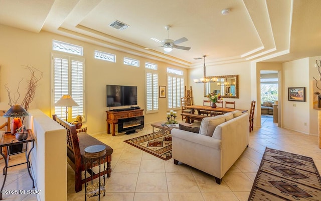 tiled living room featuring a tray ceiling, plenty of natural light, and ceiling fan with notable chandelier