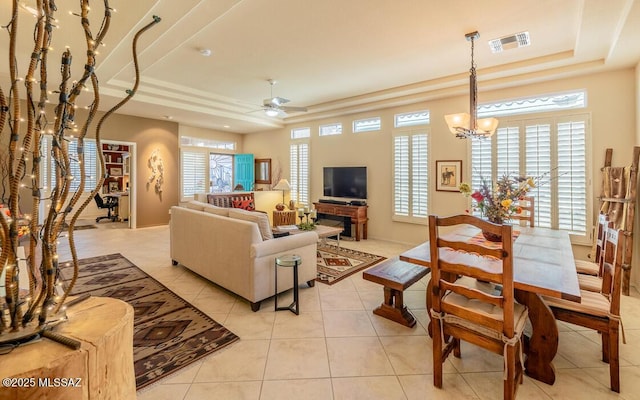 tiled living room featuring ceiling fan with notable chandelier and a raised ceiling