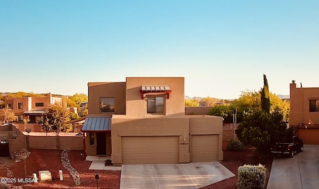 adobe home with a standing seam roof, an attached garage, driveway, and stucco siding