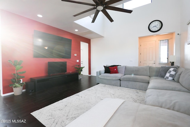 living room with baseboards, a skylight, a towering ceiling, wood finished floors, and a ceiling fan