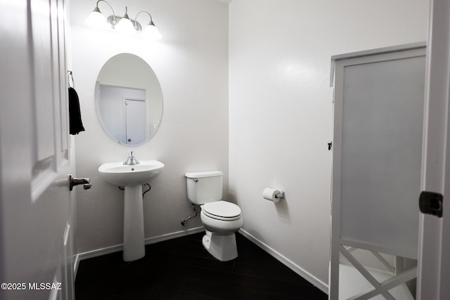 half bath with toilet, wood finished floors, and baseboards