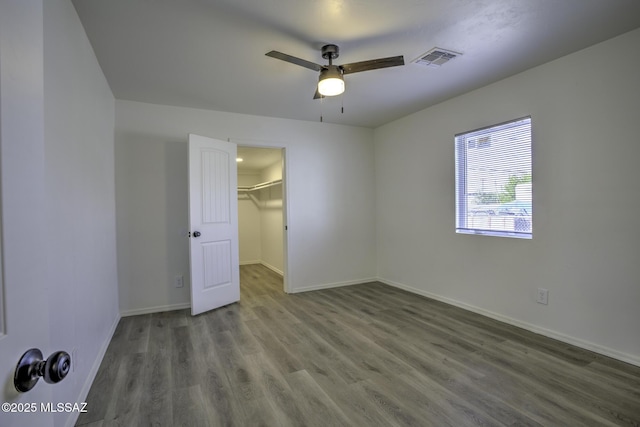 unfurnished bedroom featuring a walk in closet, ceiling fan, a closet, and wood-type flooring