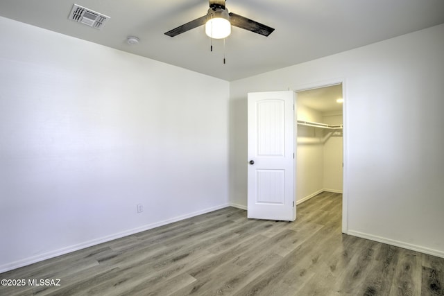 unfurnished bedroom featuring wood-type flooring, a walk in closet, a closet, and ceiling fan