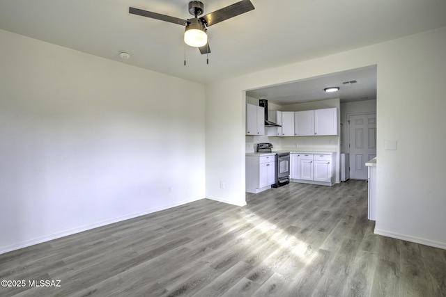 interior space with ceiling fan, wall chimney exhaust hood, black / electric stove, white cabinets, and light wood-type flooring