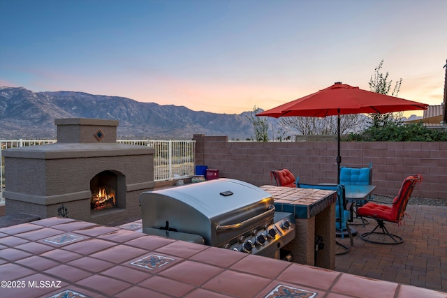 patio terrace at dusk with a mountain view, area for grilling, and exterior fireplace