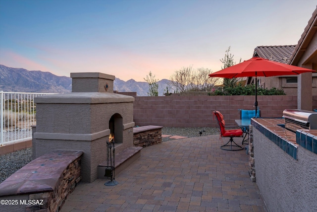 patio terrace at dusk featuring an outdoor fireplace, a mountain view, and a grill